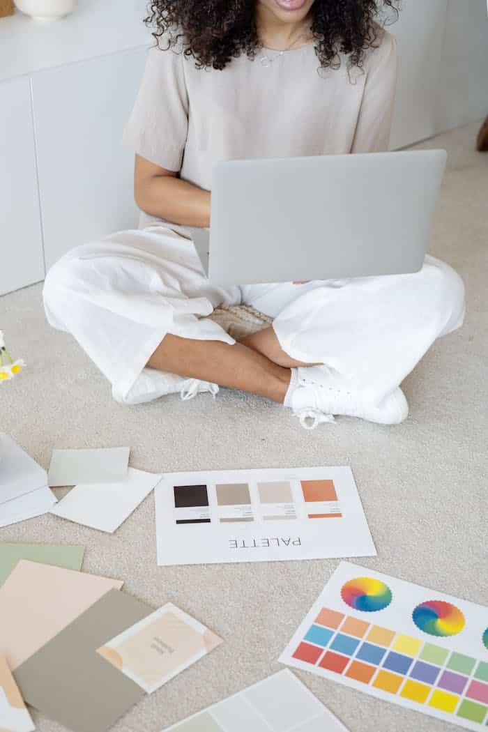 Young woman reviews color palettes for design project on laptop, sitting indoors.
